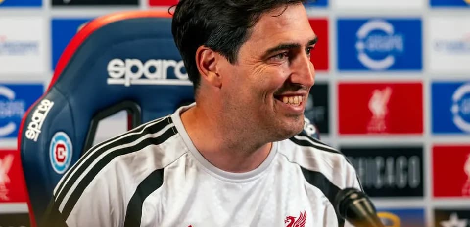 Coach speaking at press conference with Liverpool backdrop