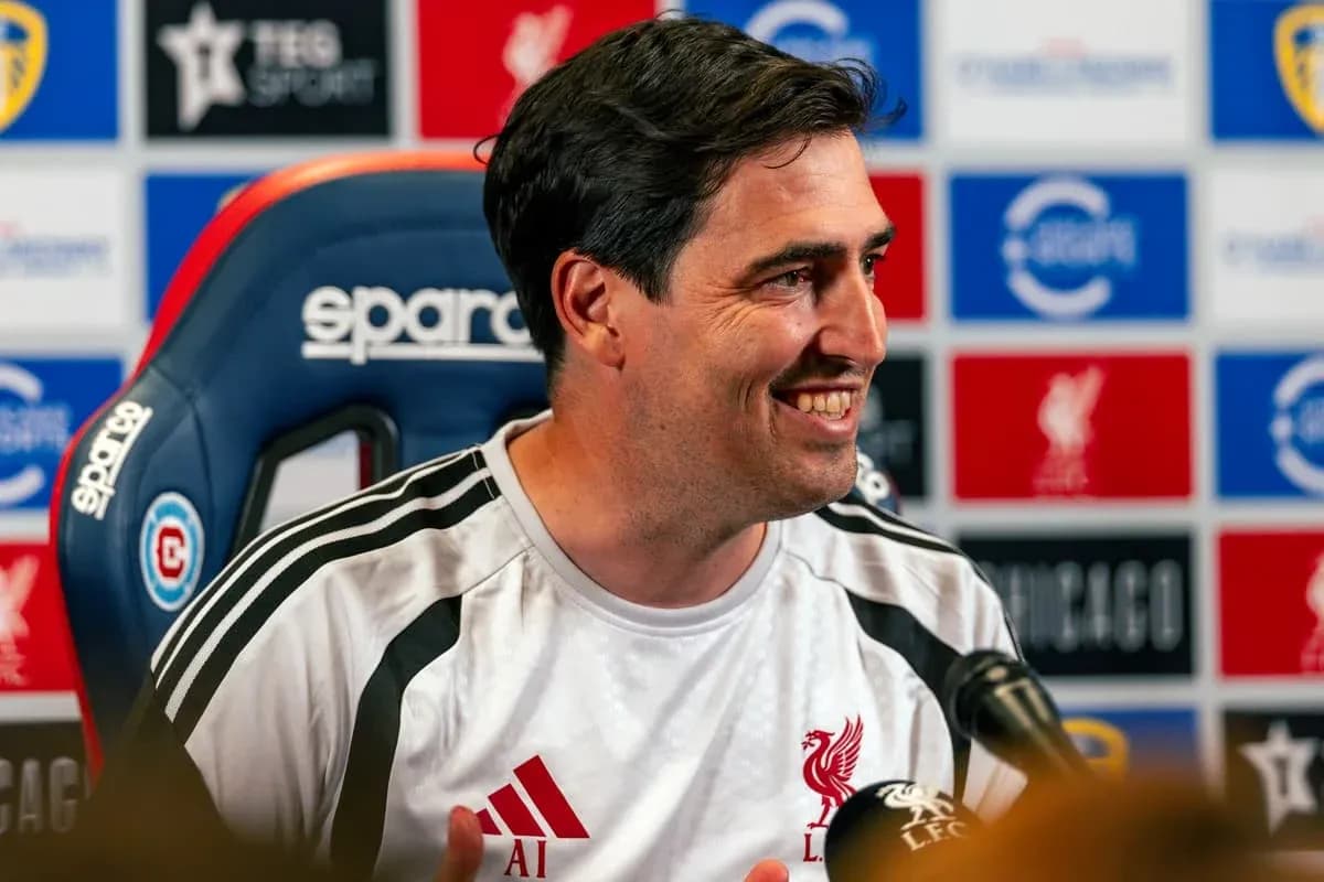 Coach speaking at press conference with Liverpool backdrop