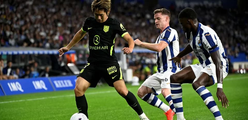 Atletico Madrid player dribbling past Real Sociedad defenders