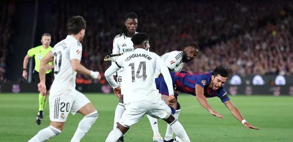 Barcelona player falling while surrounded by Real Madrid defenders