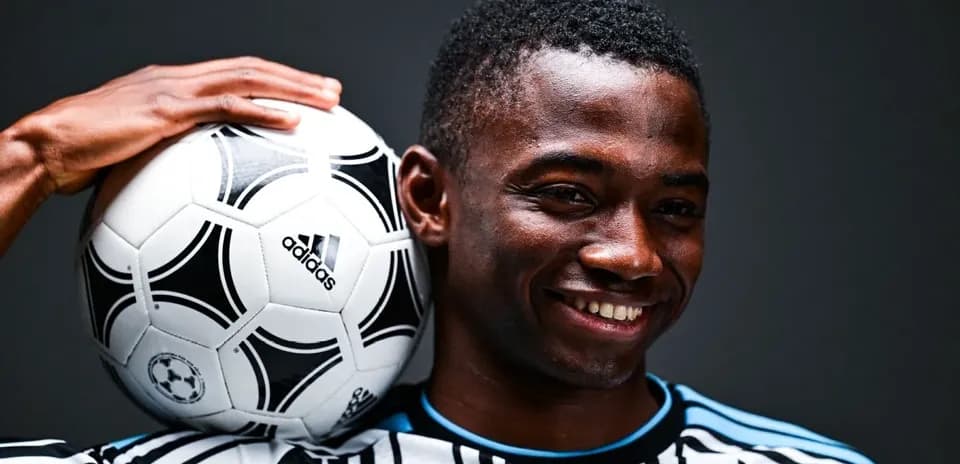 Player holding soccer ball on shoulder, smiling