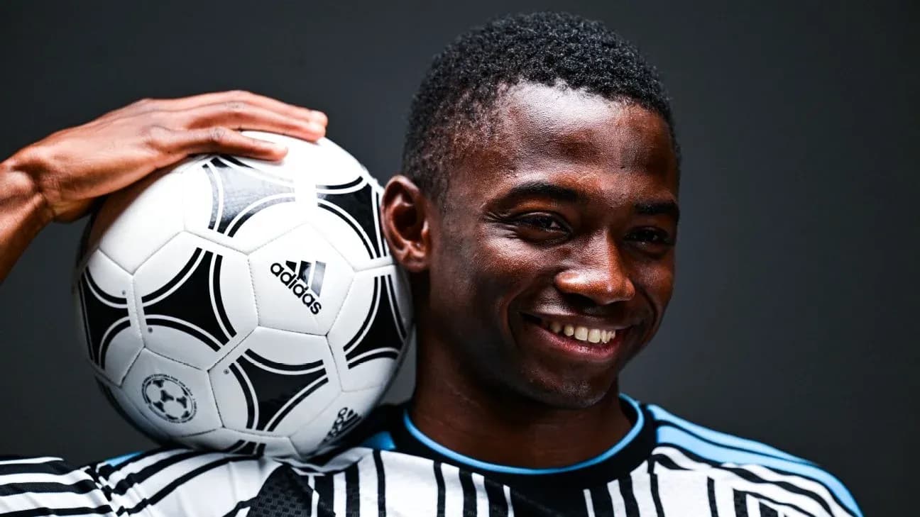 Player holding soccer ball on shoulder, smiling