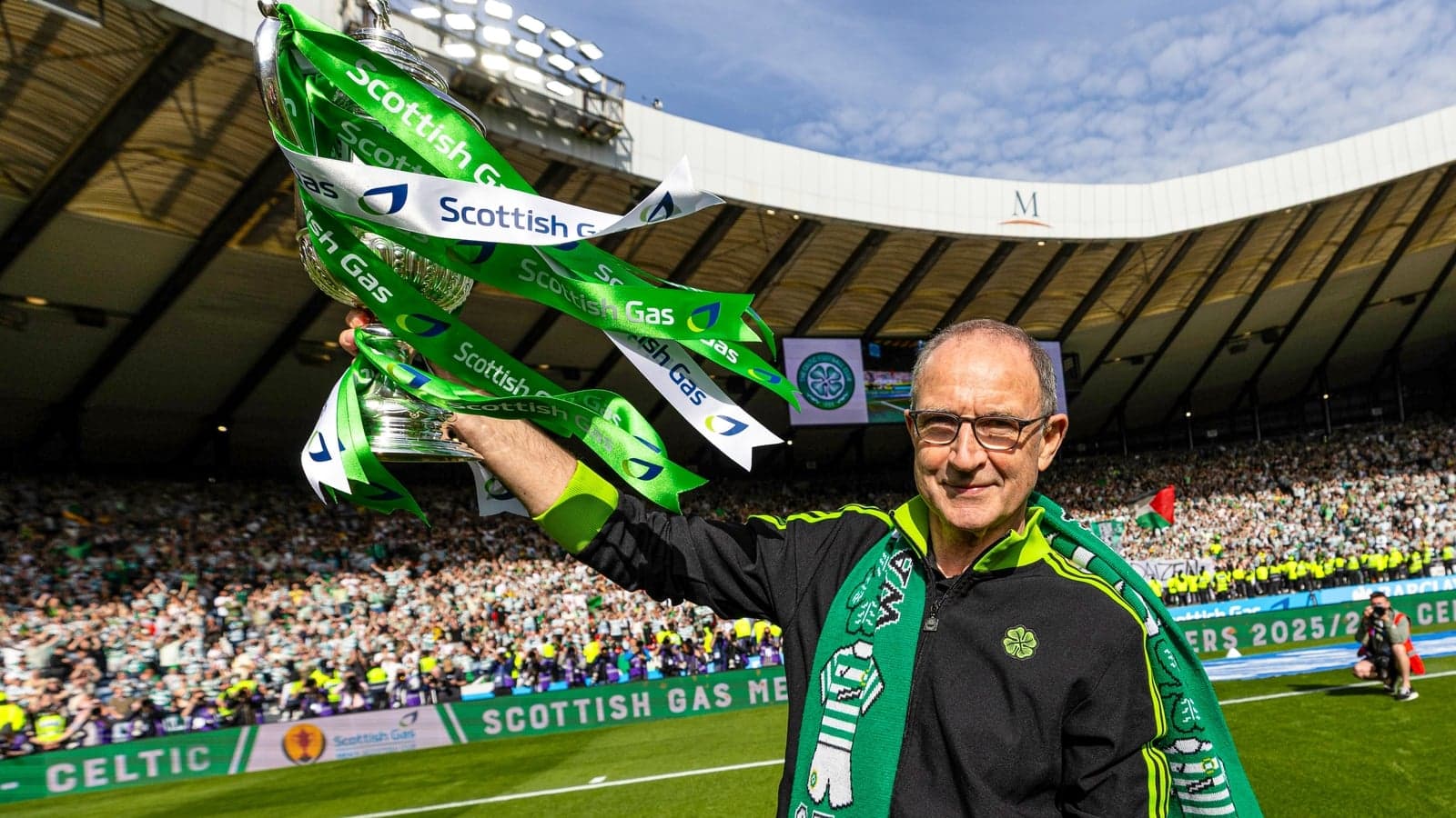 Man holding trophy with green ribbons in stadium