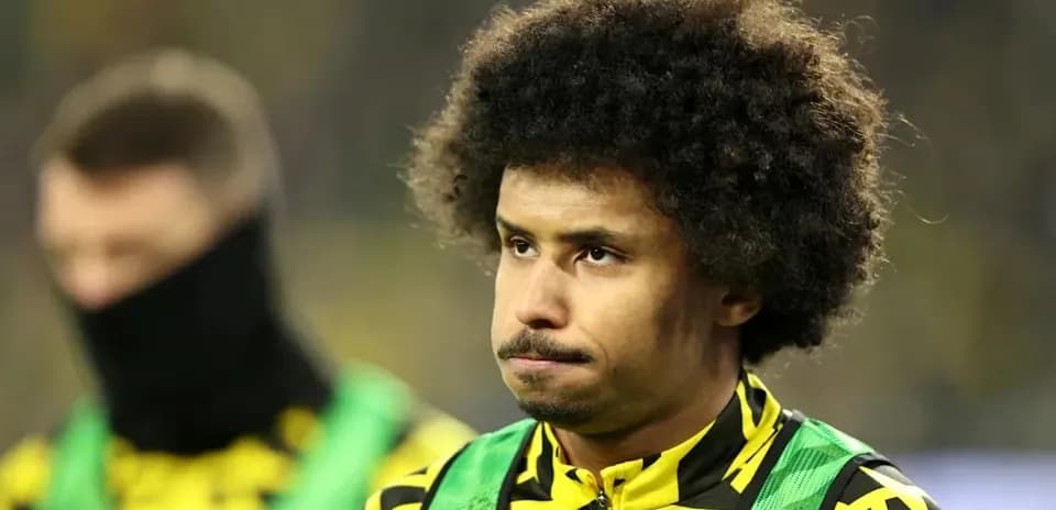 Player in yellow and black kit on the sidelines