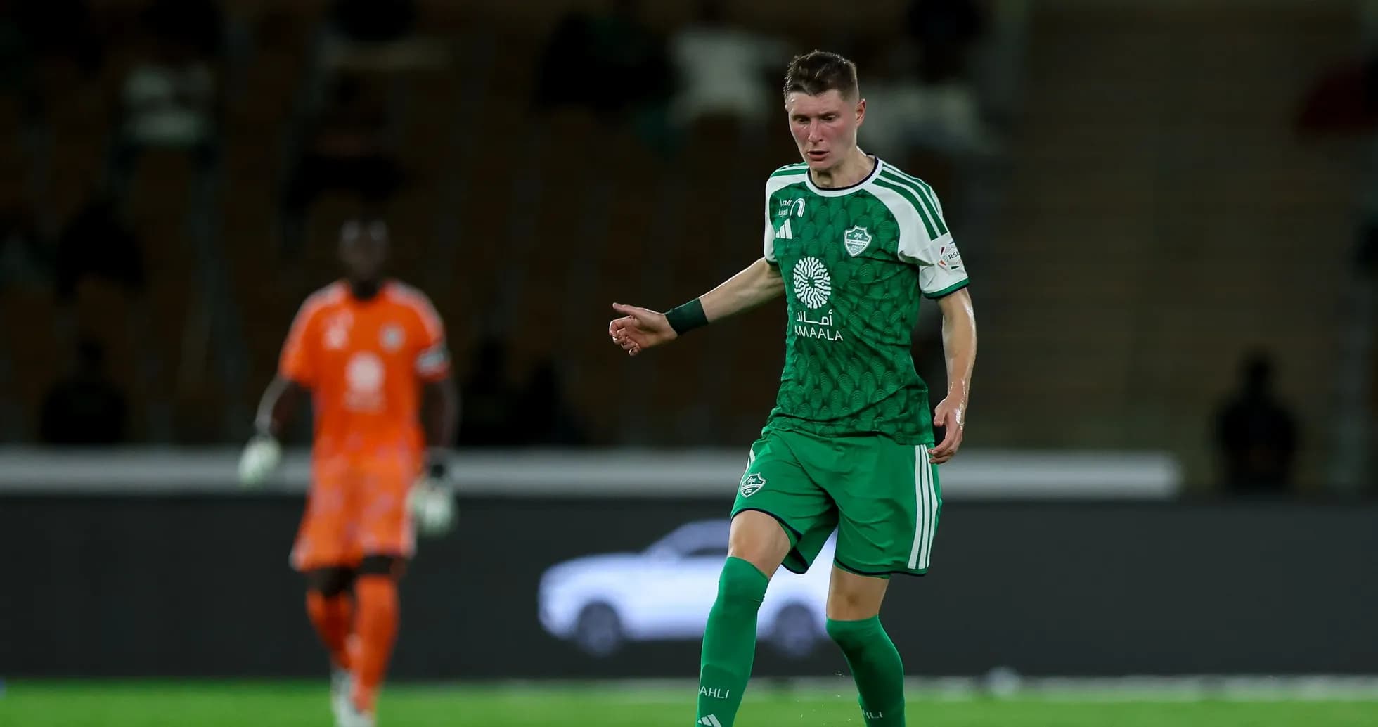 Player in green kit dribbling the ball on field