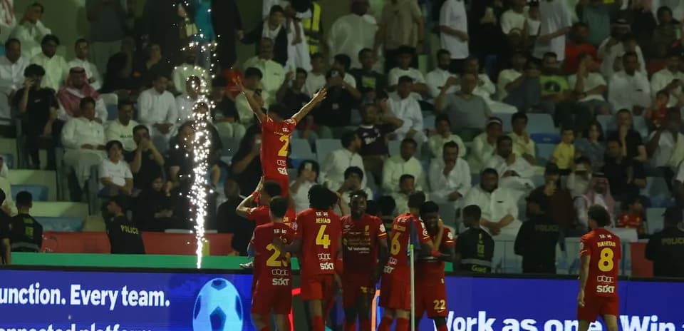 Players celebrating a goal with fireworks in stadium