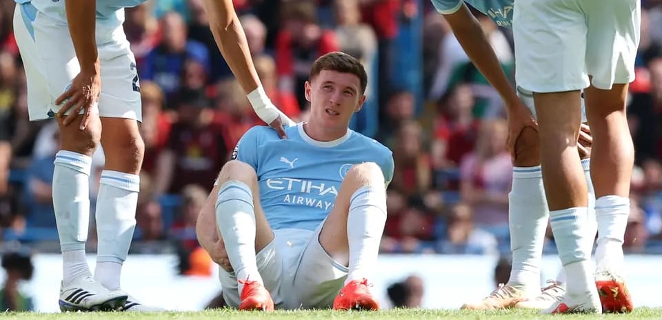 Player sitting on pitch with teammates supporting him