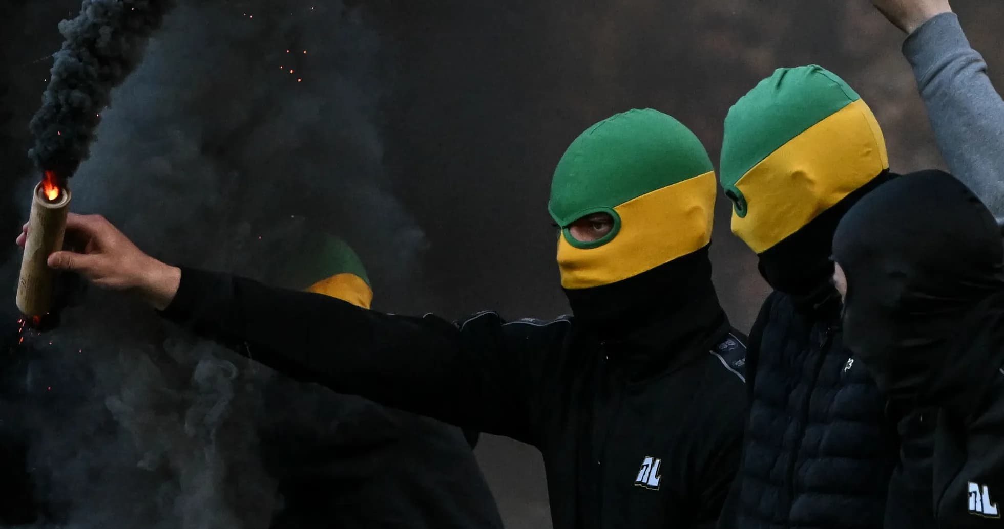 Masked individuals holding flares amidst smoke