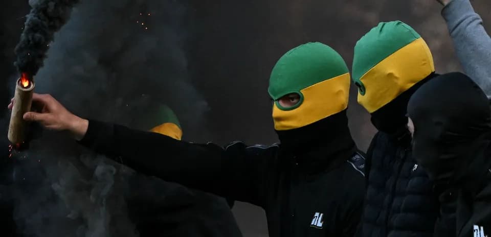 Masked individuals holding flares amidst smoke