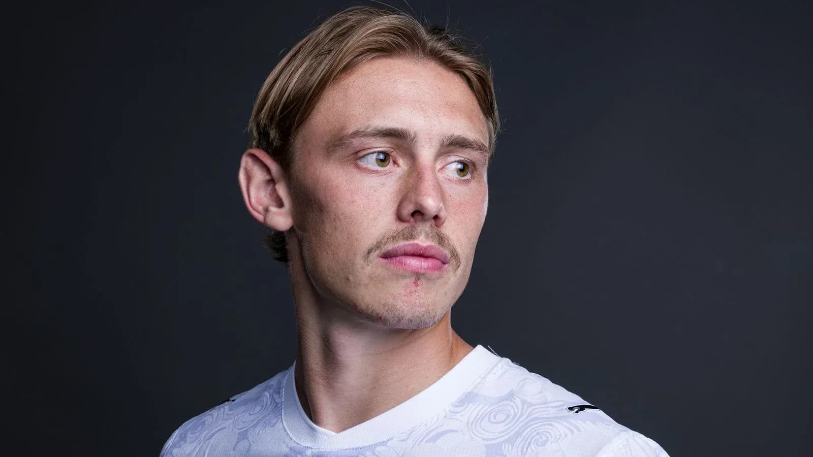 Player posing in a white jersey against dark background