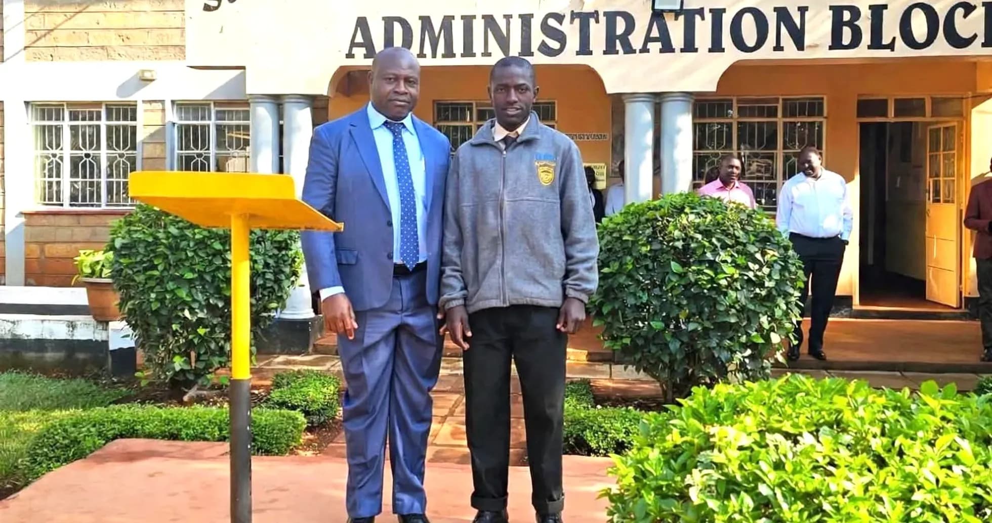 Two individuals posing outside St. Anthony's Boys' High School