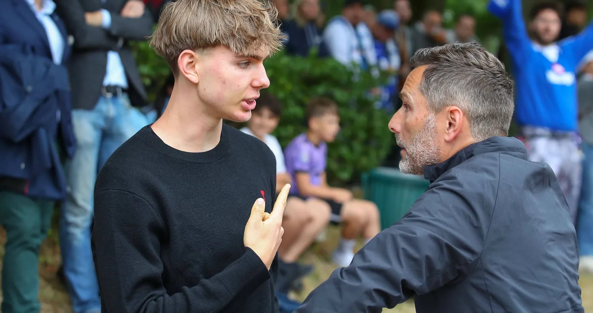 Young man and adult discussing near spectators