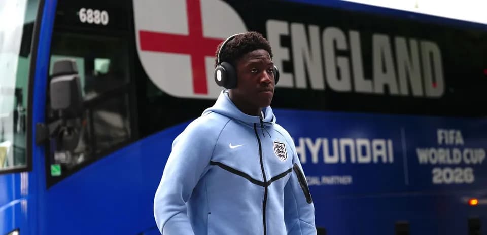 Player wearing headphones walking past England team bus