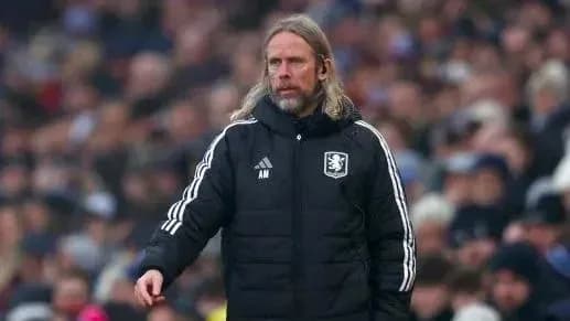 Coach in black jacket on sidelines during match
