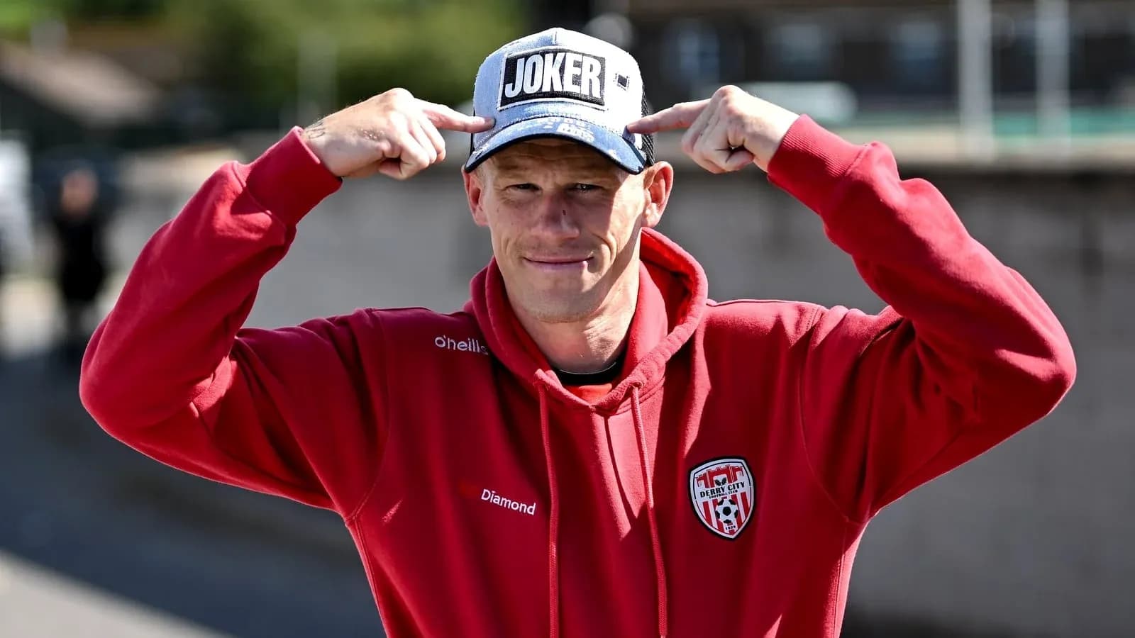 Man wearing a 'JOKER' cap and red hoodie