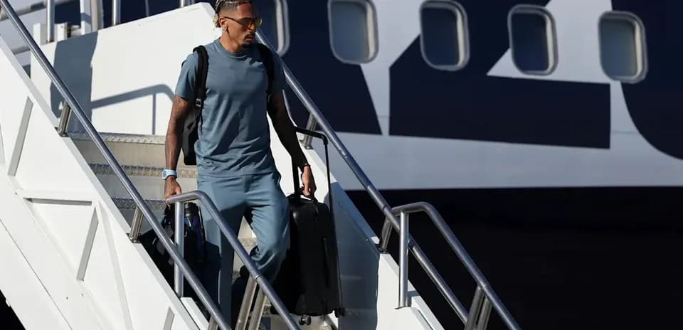 Player walking down airplane steps with suitcase