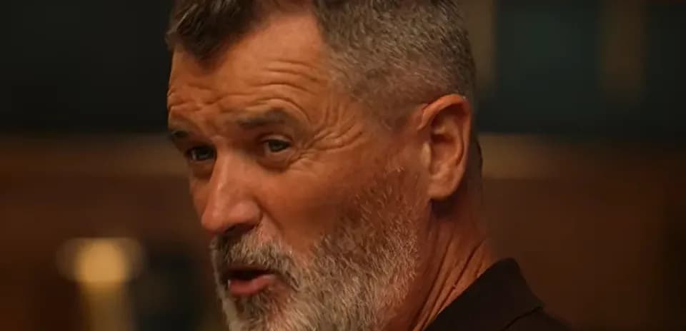 Man with gray beard speaking in a dimly lit room