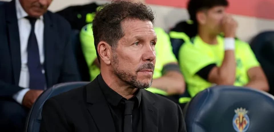 Coach seated on bench during match with players behind