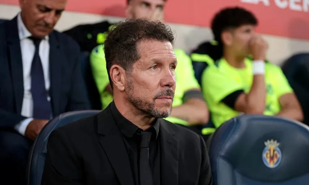 Coach seated on bench during match with players behind