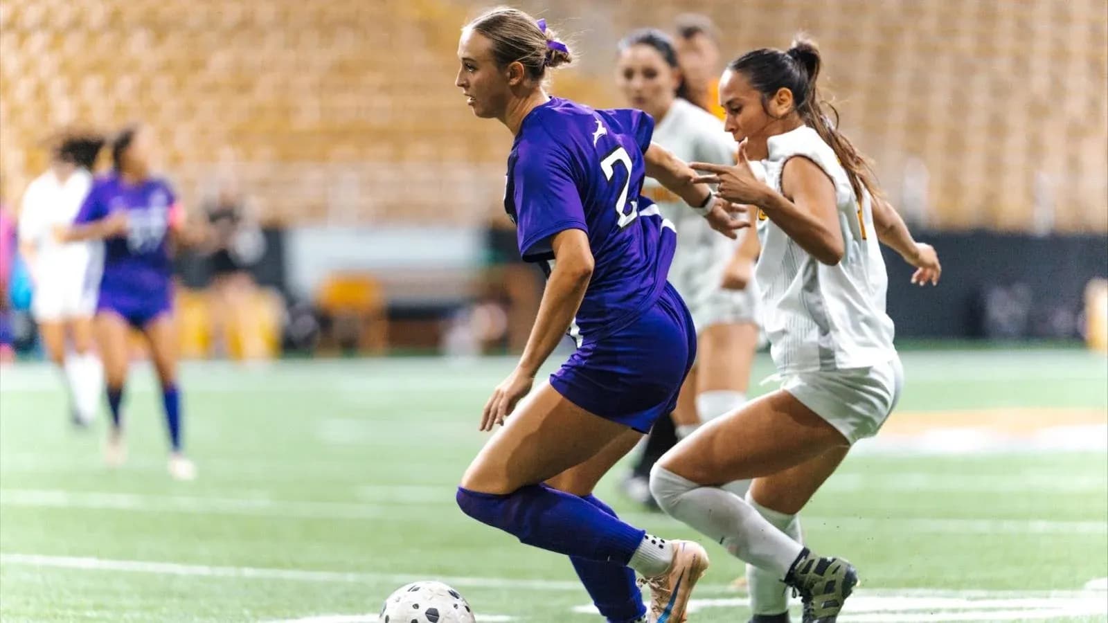 Player in purple dribbling past opponent in white