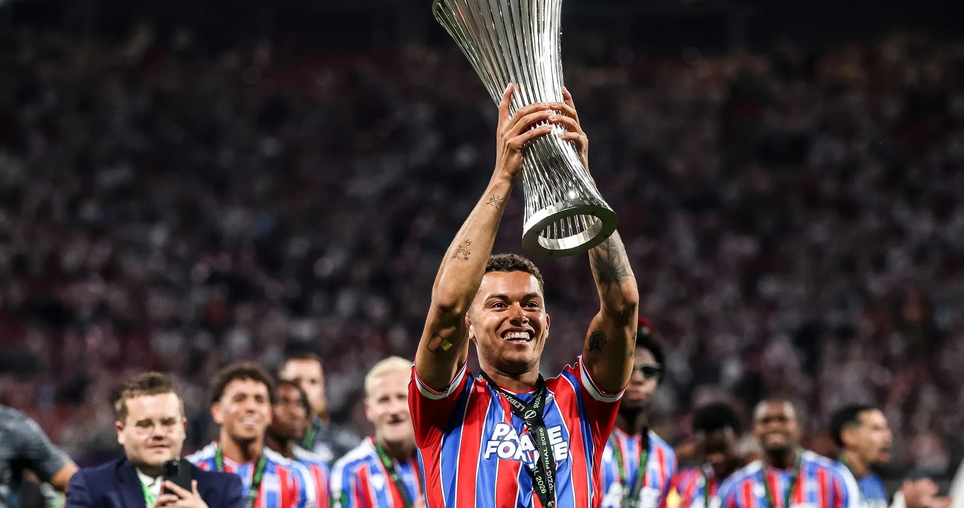 Player holding trophy with team celebrating in background
