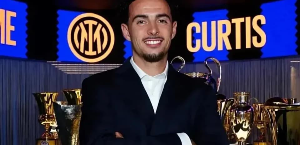 Man in suit smiling with trophies in background