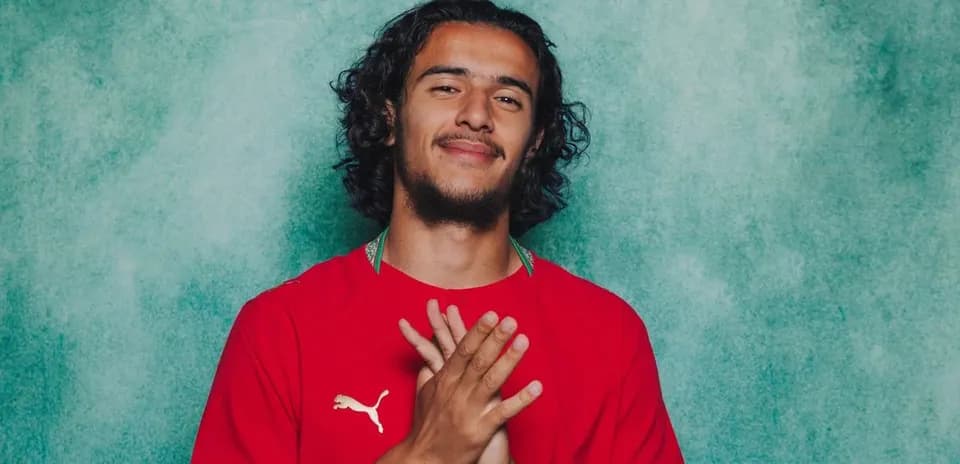 Player posing in red jersey against teal background