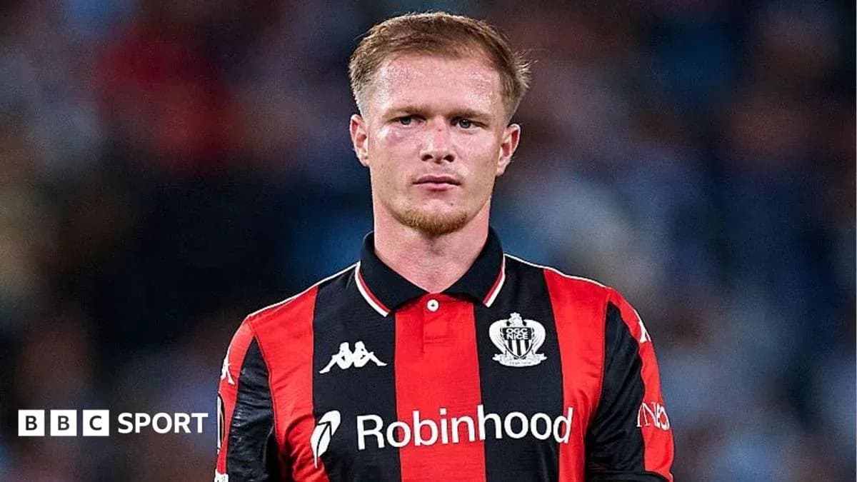 Player in black and red kit on field Player in black and red kit on field