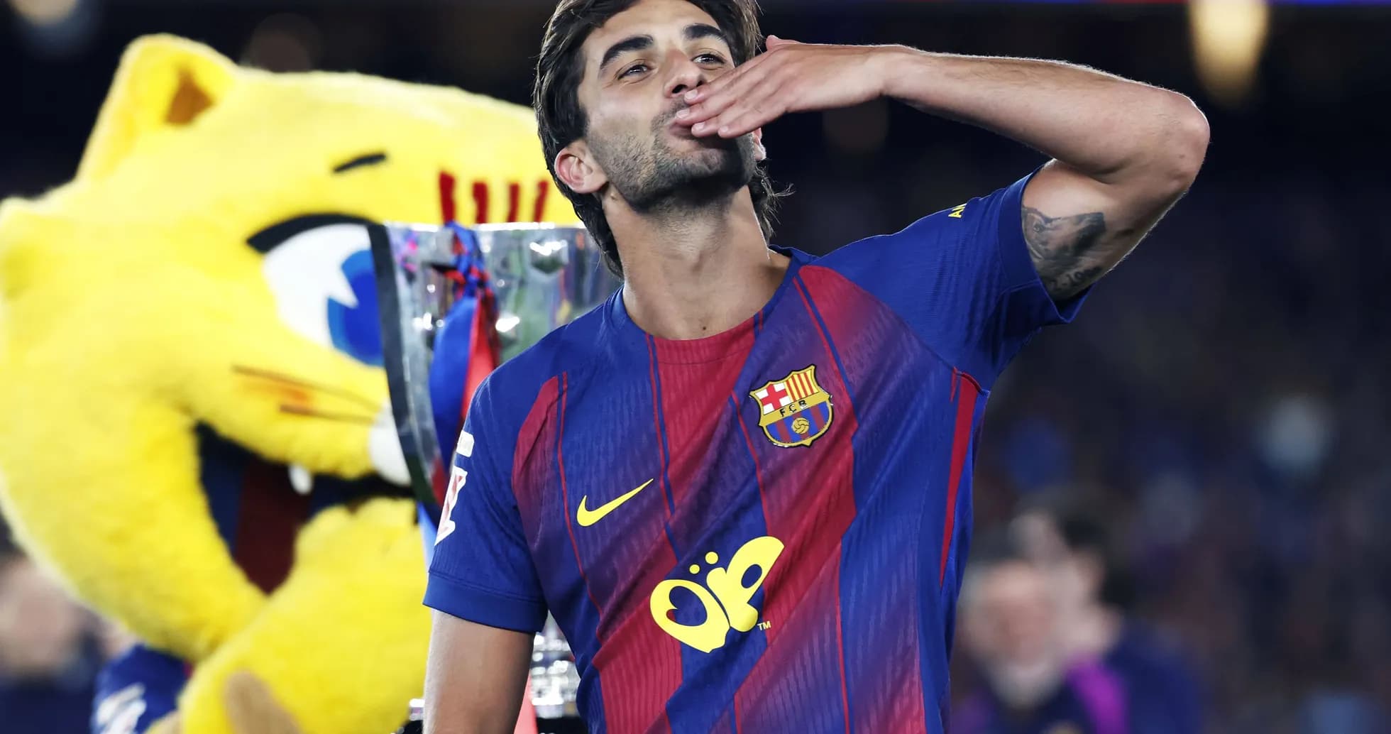 Player celebrating with trophy and mascot in background Player celebrating with trophy and mascot in background
