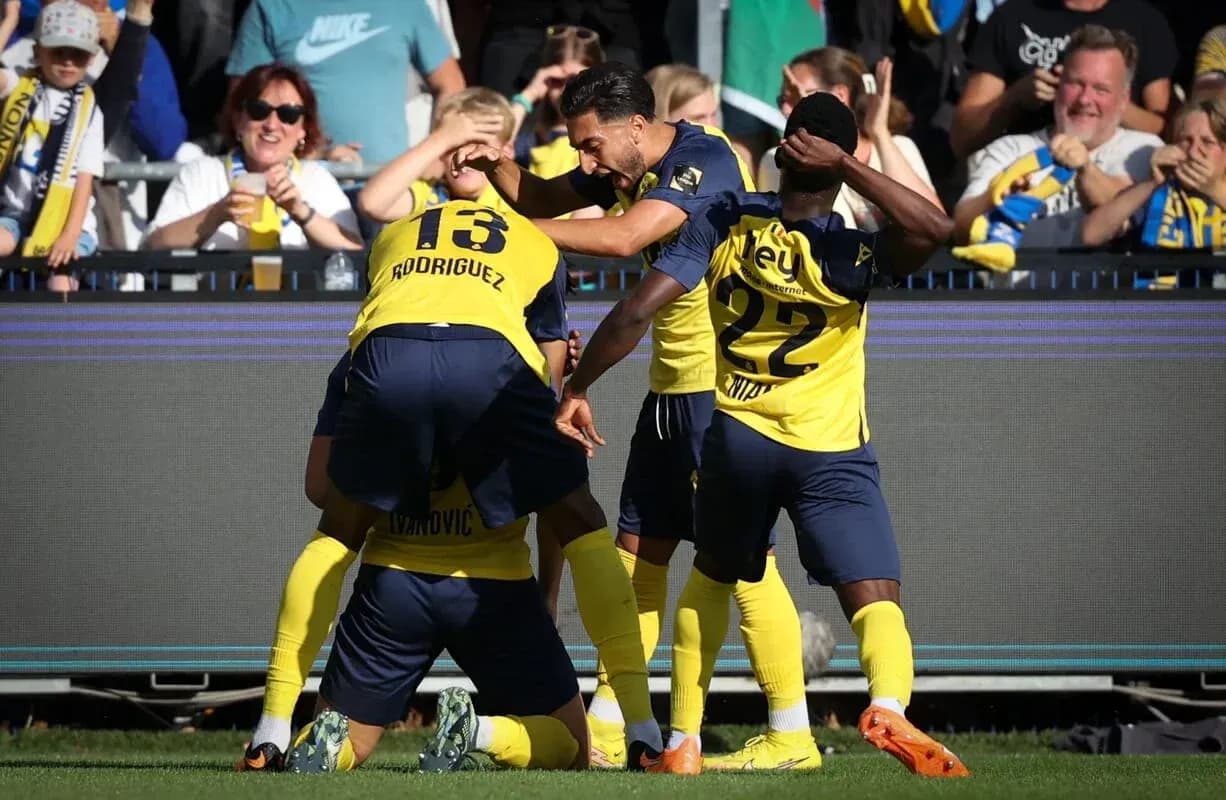 Players celebrating a goal with fans in background Players celebrating a goal with fans in background