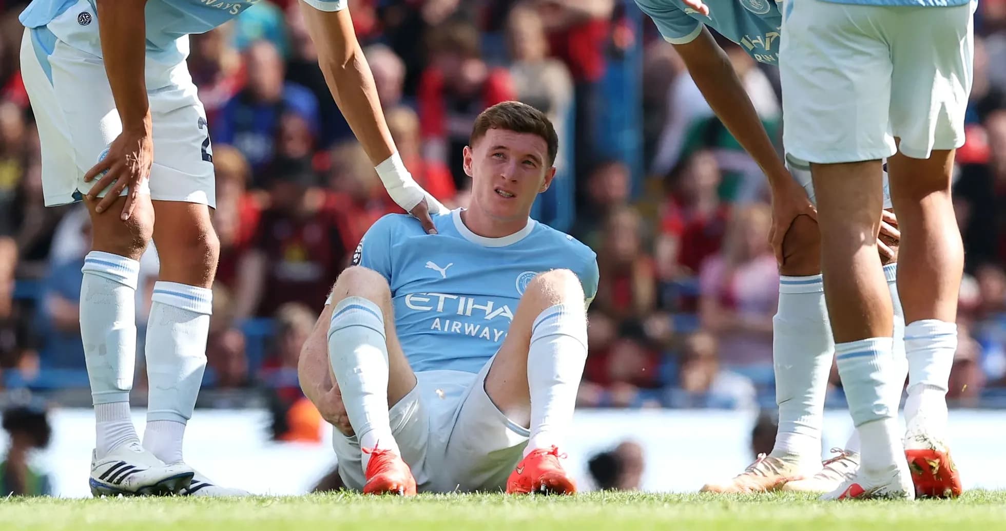 Player sitting on pitch with teammates supporting him Player sitting on pitch with teammates supporting him