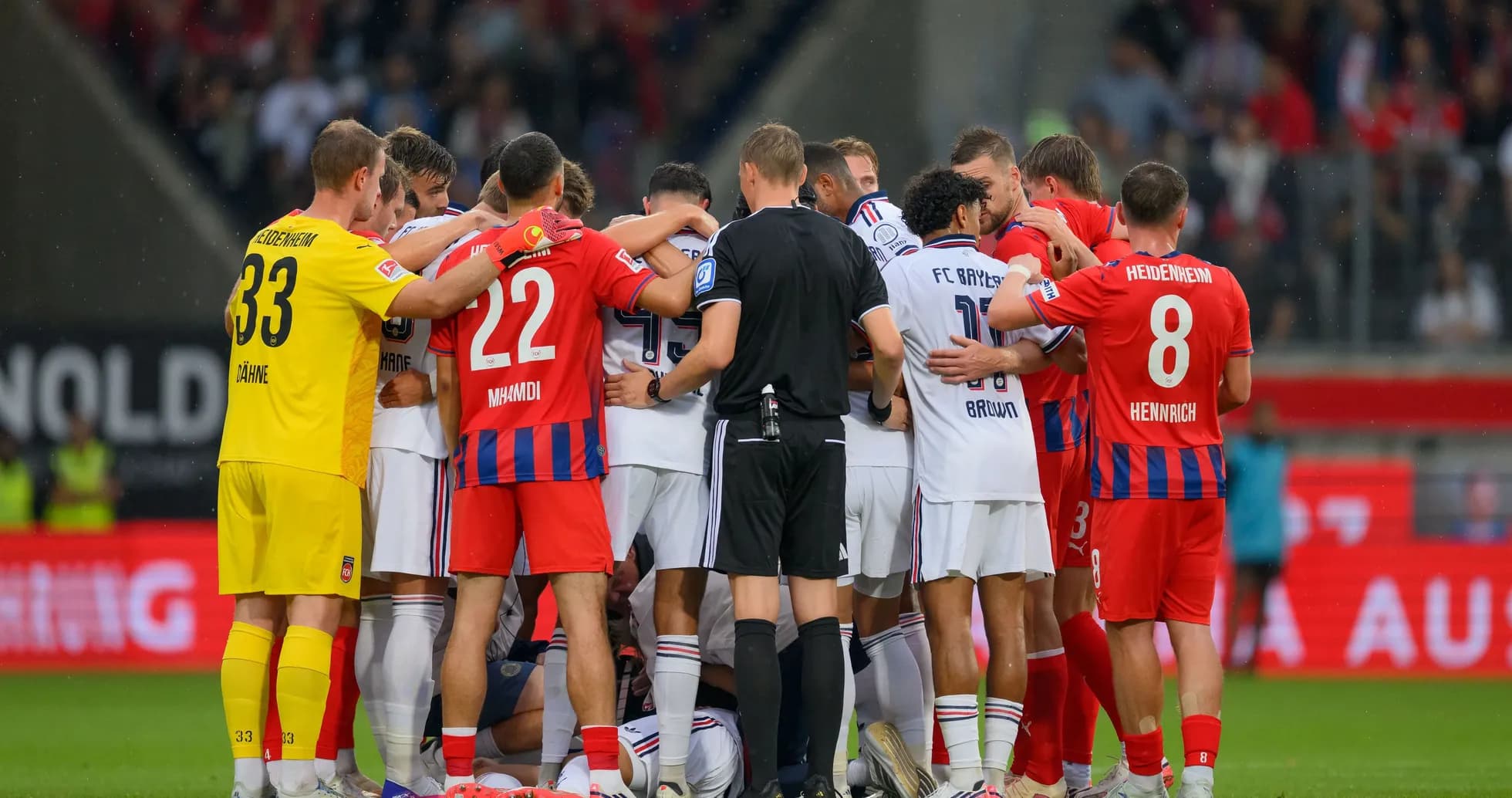 Players from both teams huddled together on the pitch Players from both teams huddled together on the pitch